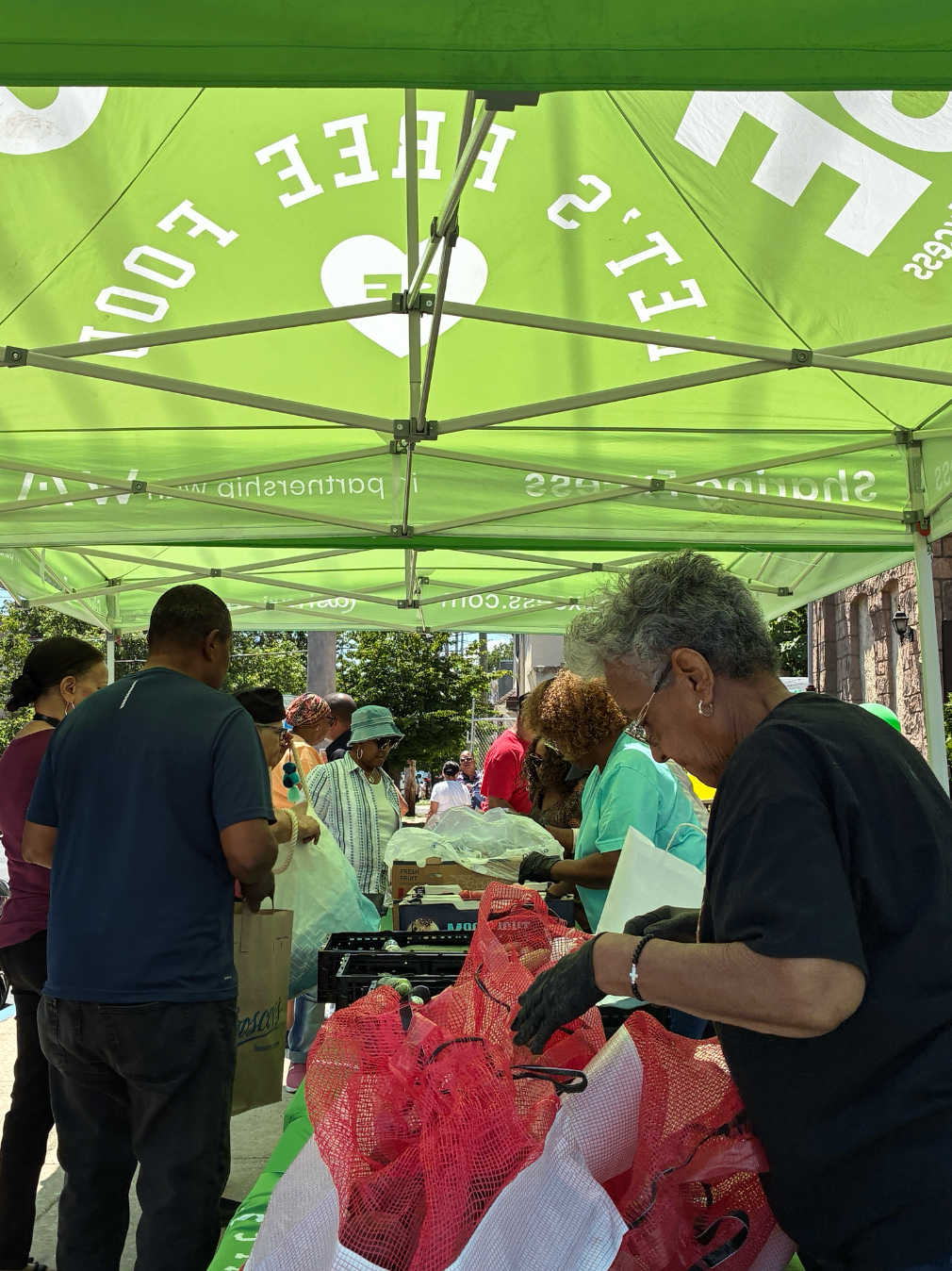 Neighbors selecting rescued produce under a Sharing Excess canopy during a pop-up distribution