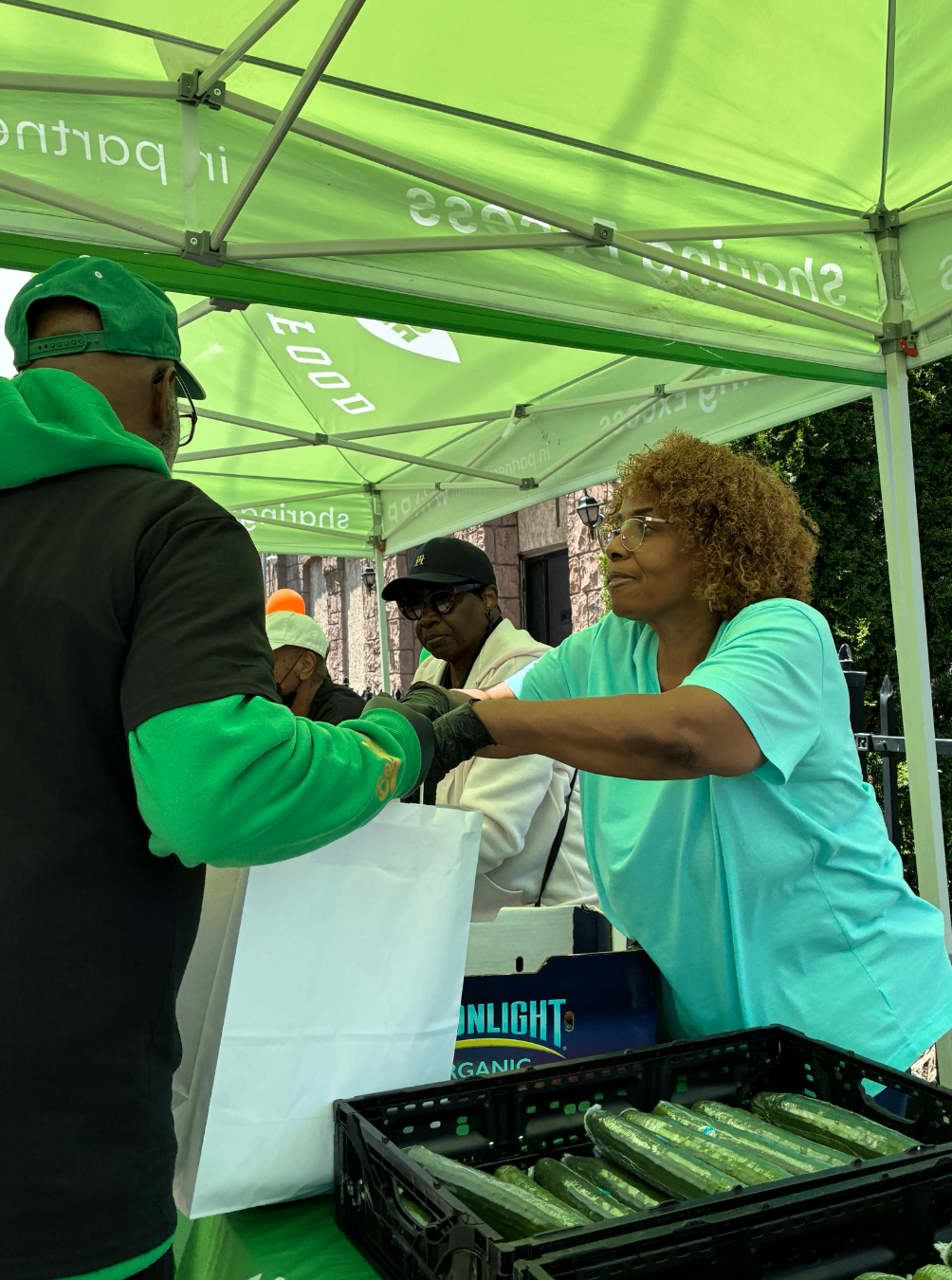 Volunteer handing produce to a neighbor at a Sharing Excess pop-up distribution